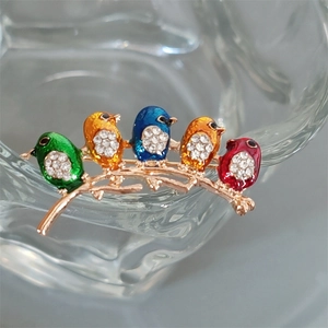 Close-up of five colorful enamel birds with sparkling rhinestones on a golden branch