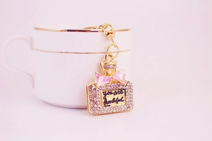 Detail eines Strass-Parfümflaschen-Schlüsselanhängers mit rosa Schleife an Kaffeetasse