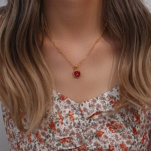 Detail of a paperclip chain necklace with a square red zircon pendant on a model neck