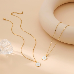 Minimalist gold sun and moon necklaces with white enamel pendants on cream background