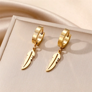 Macro shot of gold feather pendant hoop earrings on a luxury beige jewelry box