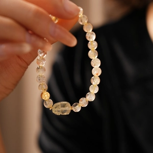 Detail of beaded rutilated quartz bracelet featuring a golden coin charm and carved gem