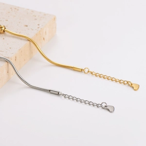 Elegant gold and silver snake chain bracelets with heart pendants on a textured stone