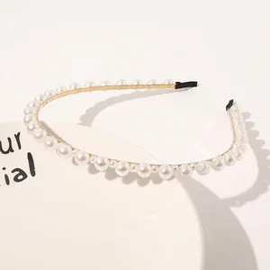 Detailed close-up of a slim gold metal headband with elegant white pearls on a ceramic plate