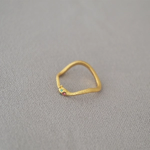Detailed macro shot of a gold snake ring featuring emerald and ruby colored gemstone eyes