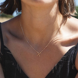 Gros plan d'un collier doré avec pendentif lettre X porté par un mannequin femme