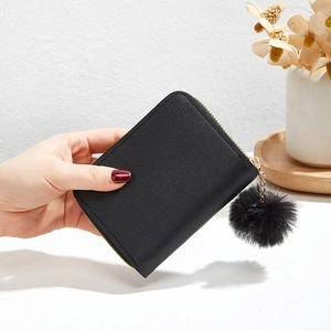 Mini black leather wallet with golden zipper and fluffy pompom charm held in hand