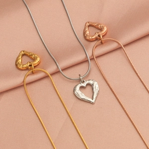 Three heart pendant necklaces in gold, silver, and rose gold on pink silk background