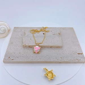 Detail of gold plated turtle pendant with pink enamel and sparkling zircon inlay
