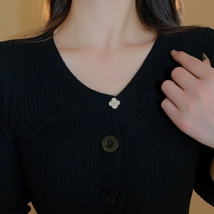 Detailed view of a gold-plated clover brooch with zircons pinned to a black knit collar