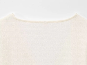 Dettaglio della trama a pieghe plissé su un top color bianco crema con scollo a barchetta