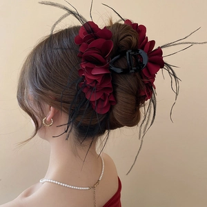Detail of burgundy floral hair claw with feathers on elegant updo hairstyle
