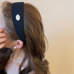 Détail d'un serre-tête en tissu noir avec bouton décoratif blanc sur le profil du modèle