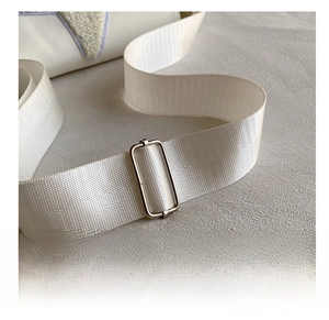 Detail of adjustable nylon strap and silver metal buckle on a white crossbody bag