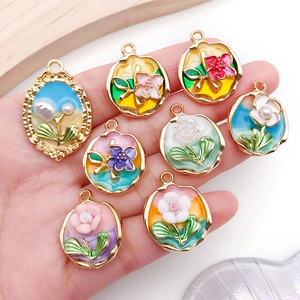 French vintage enamel flower pendants with gold borders and pearl accents in palm