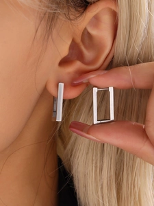 Detail shot of silver rectangular geometric hoop earrings worn by a model