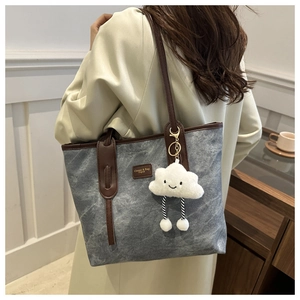 Close-up of a vintage grey tote bag with brown straps and a cute white plush pendant