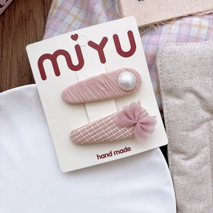 Detailed view of pink fabric bow hair clips set with white pearl on a display card