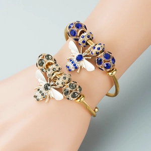 Detail of bee charm bracelets in gold finish with blue and grey crystal beads on wrist