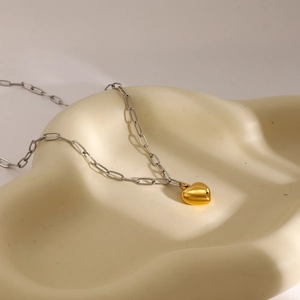 Close-up of a two-tone 18k gold heart pendant on a silver paperclip chain necklace