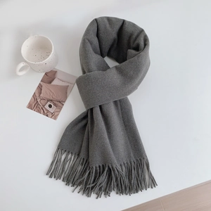 Detailed view of grey cashmere-feel scarf with elegant fringes on a minimalist desk