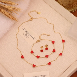 Elegant gold stainless steel jewelry set with red heart pendants on a beige tray