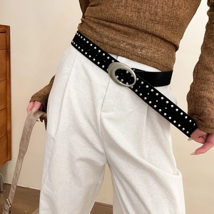 Détail des rivets argentés à double rangée sur une large ceinture punk en cuir noir