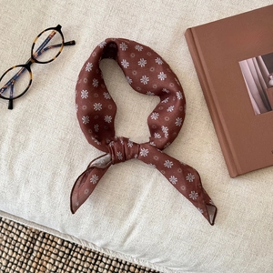 Close-up of brown floral silk scarf tied elegantly with glasses and a book on a beige background
