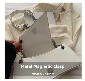 Close-up of the secure silver magnetic hardware clasp on a white geometric shoulder bag