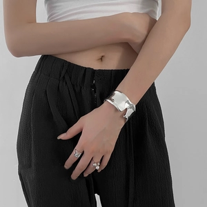 Gros plan d'un bracelet ouvert argenté irrégulier et de bagues sur un mannequin femme