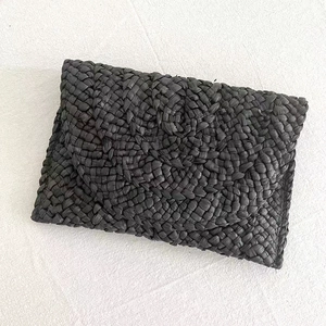Close-up of black woven raffia envelope clutch bag showing detailed straw texture