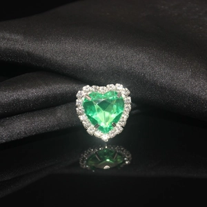Macro shot of green heart-shaped crystal ring with diamond halo on black satin background