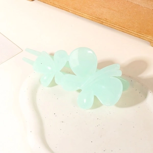 Detail shot of a matte mint green double butterfly hair clip on a white ceramic plate