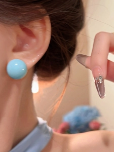 Close-up of a glossy sky blue spherical stud earring worn on an ear.