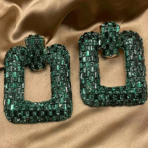 Macro detail of emerald green rhinestone geometric earrings on golden silk fabric