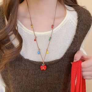Détail d'un pendentif pomme rouge sur cordon tressé marron avec des perles colorées