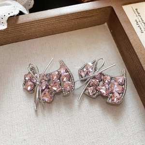 Detailed macro view of pink heart-crystal dog earrings with silver bow accents