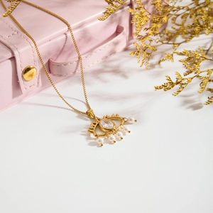 Detail of gold evil eye necklace with white zircon and small pearl fringes on pink box