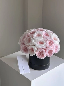 Close-up of pink and white roses in a black round floral gift box with an insert card