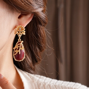 Close-up of vintage gold flower earrings with a red teardrop gem worn by a model
