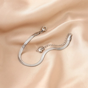 Detail of silver snake chain bracelet with heart pendant on elegant champagne silk fabric