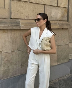 Chic white sleeveless vest and wide leg trousers set styled with a straw clutch bag
