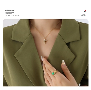 Detailed view of gold cross pearl necklace and emerald ring on a green suit model