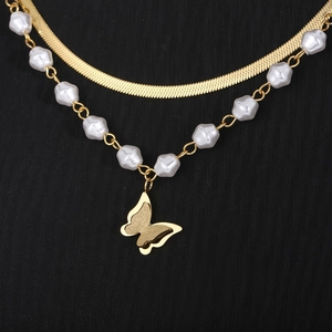 Macro detail of golden double-layer necklace with snake chain and butterfly pearl charm