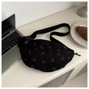 Detail of black corduroy crossbody bag with strawberry print next to a laptop