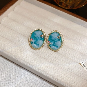 Gros plan de boucles d'oreilles camée vintage en résine bleue avec bordure perlée dorée et strass
