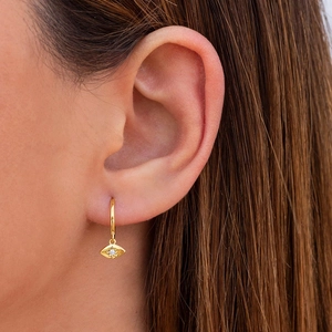 Macro detail of gold-plated evil eye hoop earring with sparkling zircon on a model