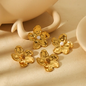 Elegant gold flower earrings with pearls and hammered texture on beige fabric background