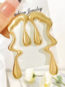 Close-up of golden liquid metal earrings with irregular drop design on jewelry card