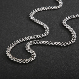 Close-up of a silver polished stainless steel Cuban link chain on a dark textured surface